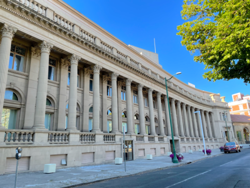 A grand, classical-style building with tall columns and large windows, set against a clear blue sky.
