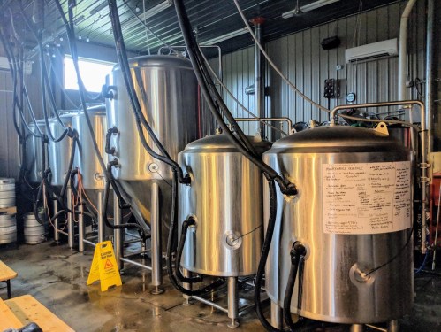 Interior of a brewery featuring several large stainless steel fermentation tanks and brewing equipment.