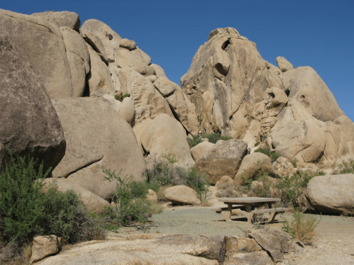Rocky landscape with large boulders and a picnic table under a clear blue sky.