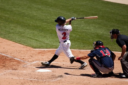A baseball player swings at a pitch while a catcher and umpire watch from behind home plate.