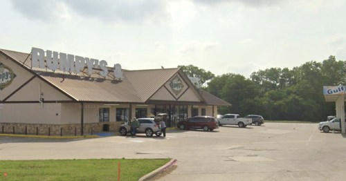 A convenience store named "Rumpy's" with a parking lot and several vehicles outside, surrounded by trees.