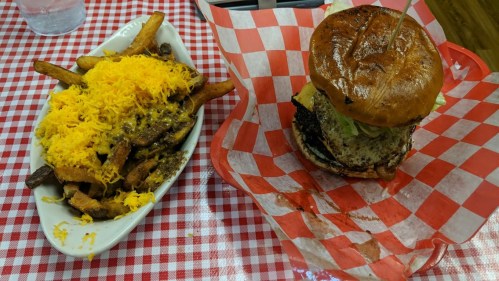 A plate of loaded fries topped with cheese next to a burger with lettuce and tomato on a checkered tablecloth.