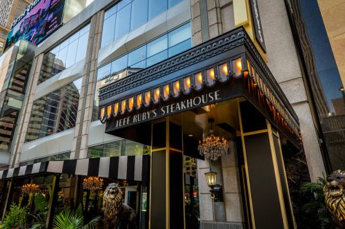 Exterior of Jeff Ruby's Steakhouse, featuring a stylish entrance with chandeliers and a black and white awning.