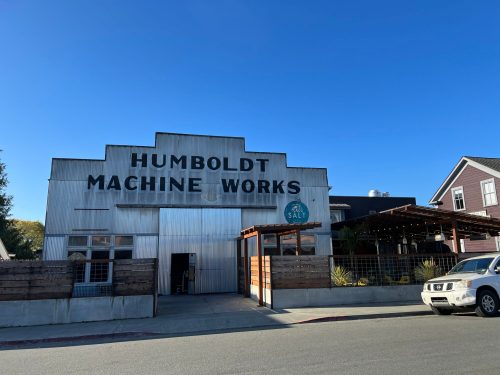 Exterior of Humboldt Machine Works building with a clear blue sky, featuring a wooden entrance and nearby parked car.