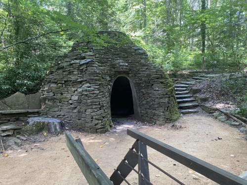 A stone structure resembling a kiln, surrounded by trees, with a pathway and steps leading up to it.