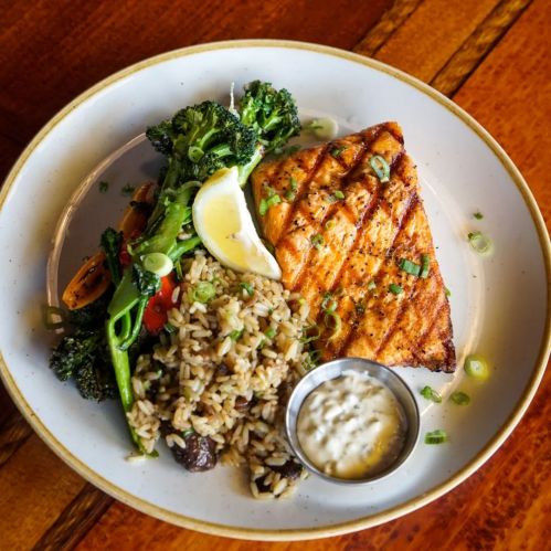 Grilled salmon fillet with rice, sautéed broccoli, lemon wedge, and a side of dipping sauce on a white plate.