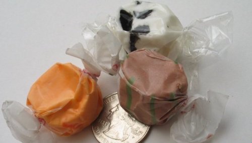 Three colorful wrapped candies next to a quarter on a white background.
