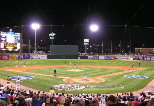 A night baseball game in a stadium, with players on the field and a crowd in the stands under bright lights.