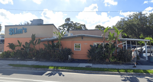 A colorful restaurant named Slim's with tropical plants outside, located on a sunny street.