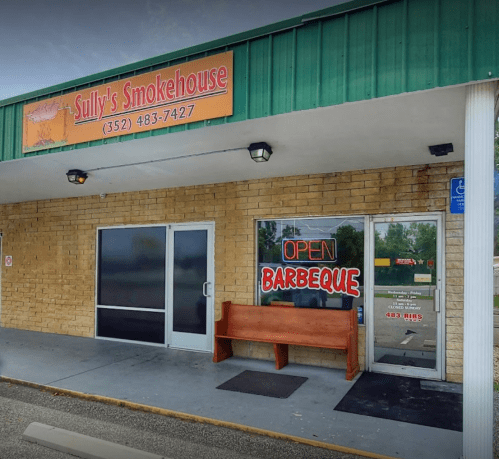 Exterior of Sully's Smokehouse with a green awning, stone walls, and an "OPEN BARBEQUE" sign on the door.