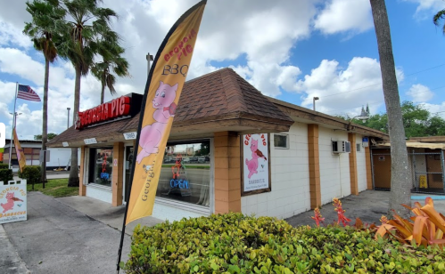 A BBQ restaurant called "George's Pig" with a colorful flag, palm trees, and a clear blue sky in the background.