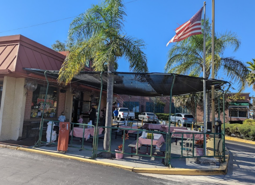 Outdoor dining area of a restaurant with palm trees, checkered tablecloths, and an American flag.