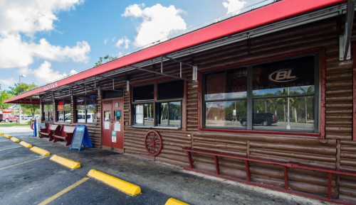 Exterior of a rustic-style restaurant with a red roof, wooden walls, and outdoor seating area.