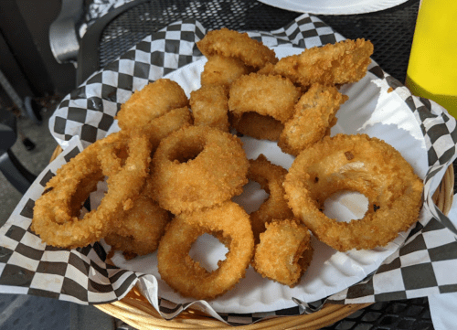 A plate of golden-brown, crispy onion rings arranged on a paper plate with a checkered border.