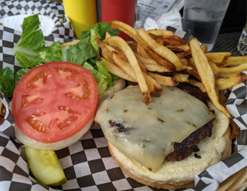 A cheeseburger with lettuce, tomato, and pickles, served with a side of fries in a checkered basket.