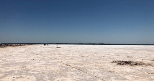 A vast, flat salt flat under a clear blue sky, with a few distant figures walking on the surface.