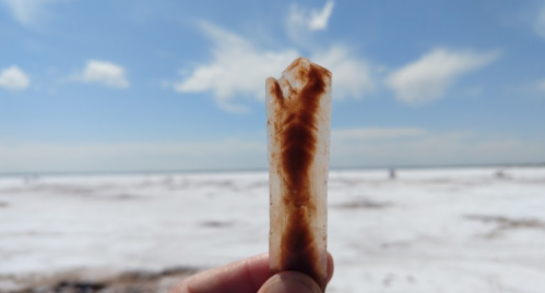 A hand holds a crystal-like mineral against a backdrop of a bright sky and snowy landscape.