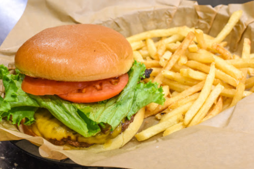 A cheeseburger with lettuce, tomato, and a side of golden French fries on a paper-lined tray.