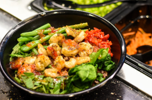 A bowl filled with shrimp, green beans, spinach, and diced tomatoes, served over rice.