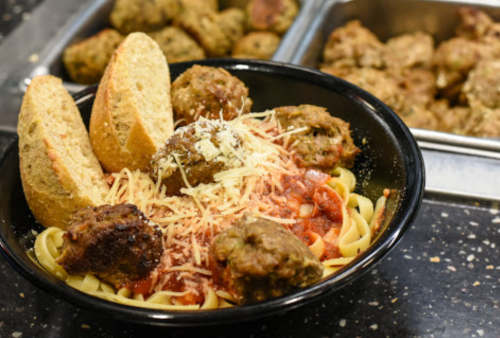 A bowl of pasta topped with meatballs, marinara sauce, grated cheese, and two slices of bread on the side.