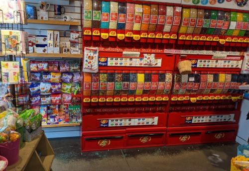 A colorful display of jelly beans in a store, with various flavors and packaging on shelves nearby.