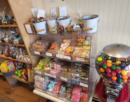 A colorful candy display with jars of sweets, a gumball machine, and assorted treats in a shop setting.
