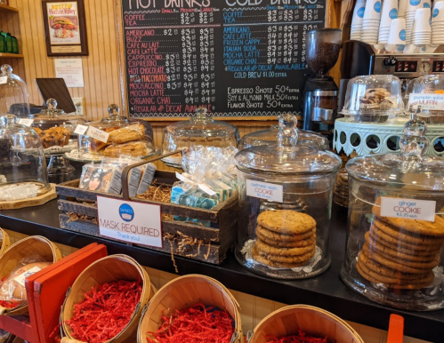 A display of baked goods in glass jars, with a menu board and a sign indicating mask requirements.