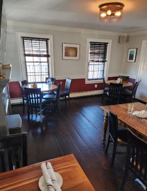 Cozy restaurant interior with wooden tables, black chairs, and large windows, featuring warm lighting and simple decor.
