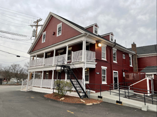 A red two-story building with white railings and stairs, set against a cloudy sky.