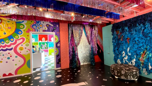 Colorful room with vibrant murals, shiny curtains, and a playful decor featuring a black and white patterned ottoman.