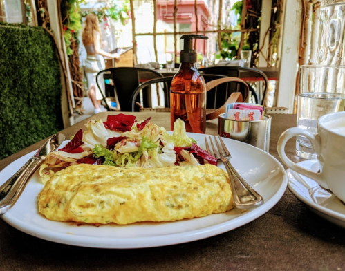 A plate with an omelette and salad, with a coffee cup and condiments on a table in a cozy café setting.
