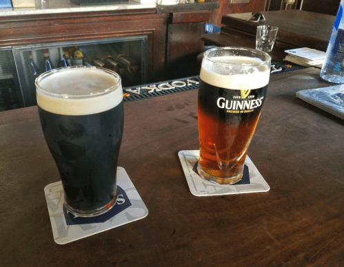 Two pints of beer on a wooden bar: one dark stout and one amber ale, both on coasters.