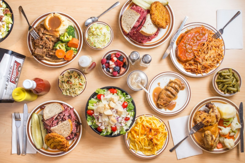A variety of dishes on a table, including salads, meats, pasta, and sides, with condiments and drinks.