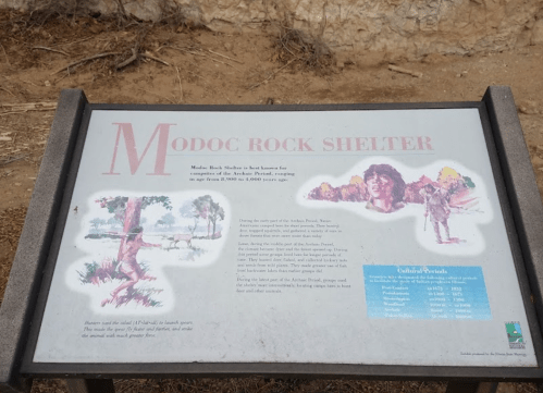 Sign about Modoc Rock Shelter, detailing its history and significance, with illustrations of the landscape and people.