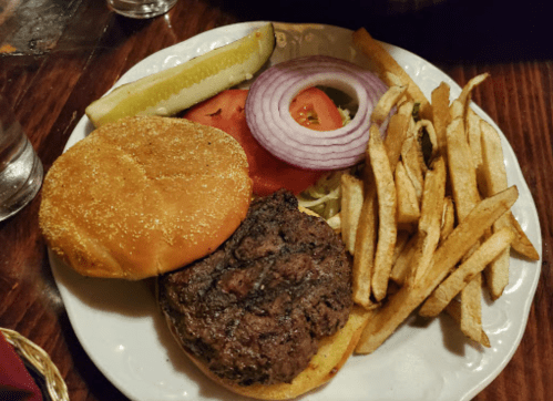 A plate with a burger patty, lettuce, tomato, onion, pickles, and a side of French fries.