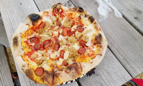 A freshly baked pizza topped with pepperoni, sausage, and melted cheese, resting on a wooden table.