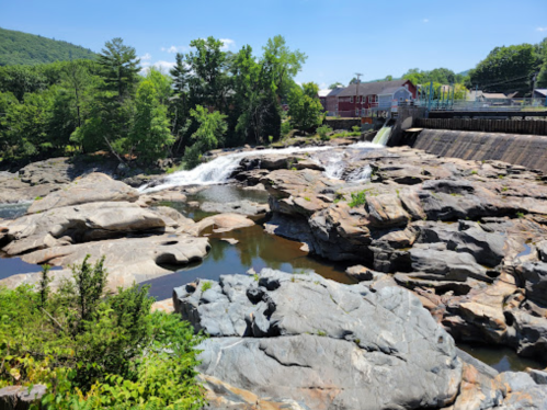 A scenic view of a waterfall cascading over rocks, surrounded by greenery and a small town in the background.