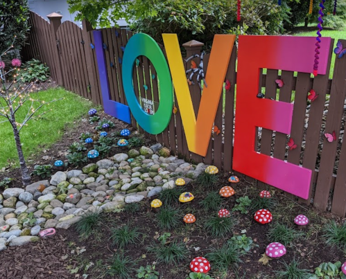 Colorful "LOVE" letters on a wooden fence, surrounded by decorative mushrooms and a landscaped garden.