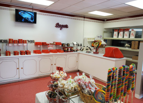 A colorful candy shop interior with a display of sweets, lollipops, and red packaging on shelves.