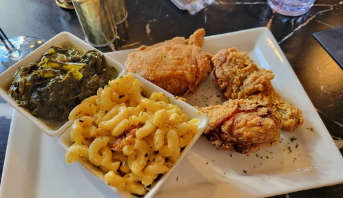 A plate featuring fried chicken, macaroni and cheese, and collard greens served in separate bowls.