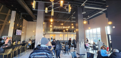 A modern café interior with stylish lighting, seating, and a motivational sign on the wall. Customers are enjoying their time.