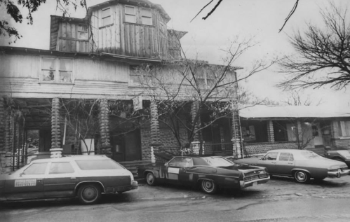 Black and white photo of a rustic wooden building with several vintage cars parked in front.