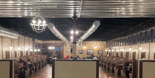 Interior of a restaurant featuring booths, metal ceiling, and warm lighting, with diners seated at tables.