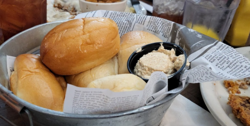 A metal basket filled with soft rolls and a small container of spread, lined with newspaper.