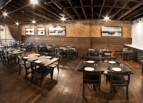 Interior of a restaurant featuring wooden tables, chairs, and exposed brick walls with black-and-white artwork.