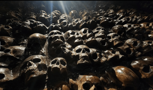 A close-up view of a wall covered with numerous human skulls, illuminated by a beam of light.
