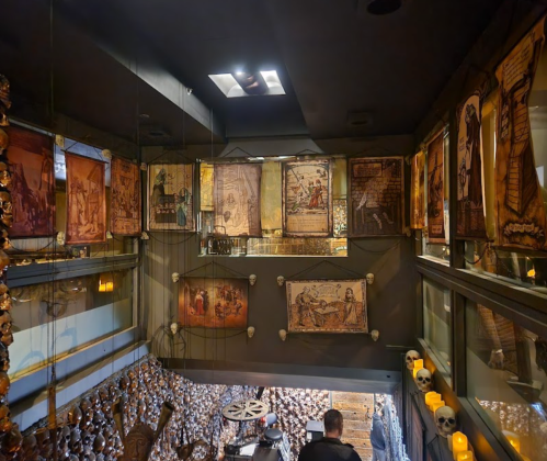A dimly lit room with skulls and framed historical illustrations on the walls, creating a macabre atmosphere.