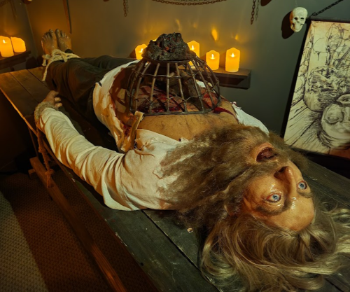 A lifelike figure on a table, with a cage on its chest and candles glowing in the dimly lit background.