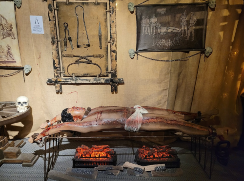 A gruesome display featuring a lifelike figure on a table, surrounded by surgical tools and historical illustrations.