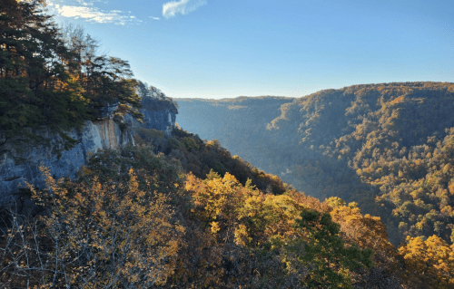 A scenic view of a valley surrounded by colorful autumn foliage and rocky cliffs under a clear blue sky.